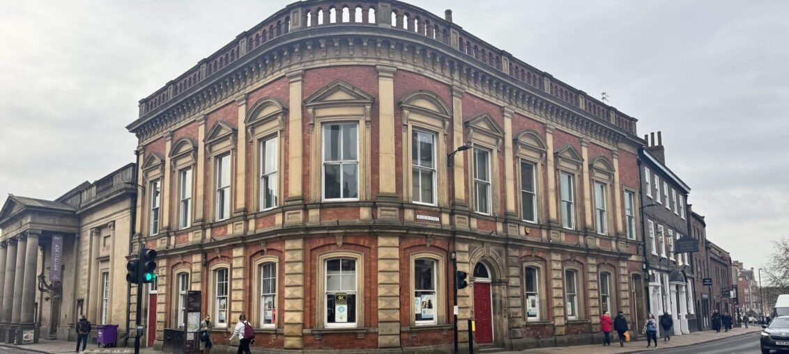 A photo of a large red building on a street corner which is becoming a bookstore.
