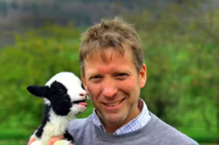 Julian Norton smiling at a camera holding a black and white lamb