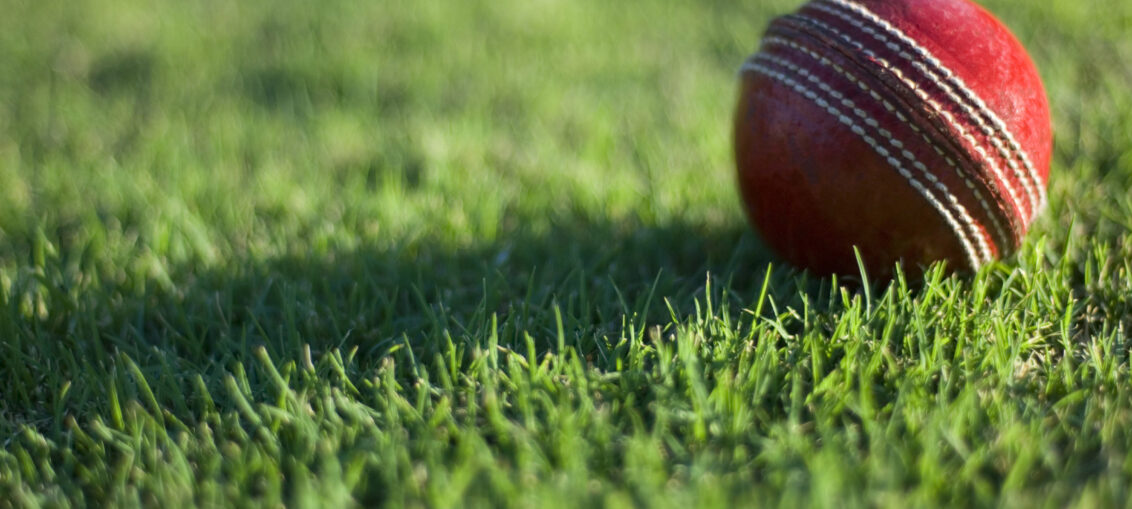 A red cricket ball lying on a field.