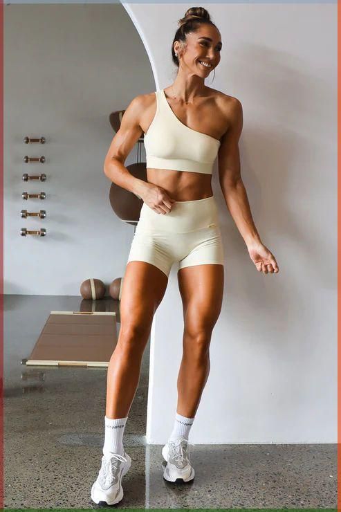 A fit woman wearing a pale yellow gym set with a one-shouldered strap. the athleisure/athlingerie aesthetics