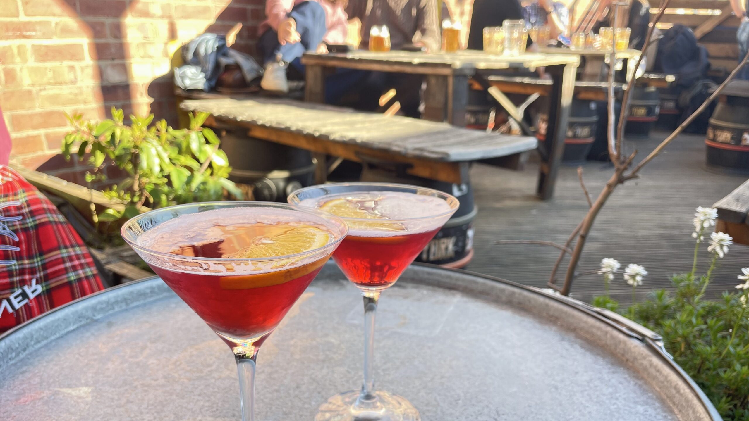 Two Cosmo cocktails in martini glasses with orange slices in them, on table in beer garden.
