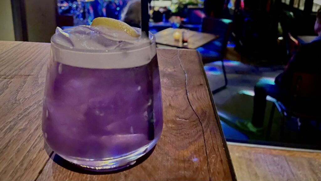 Bright purple lavender lady cocktail in a glass with a lemon on top and a foamy head.